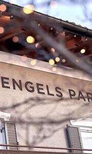 Nahaufnahme des Logos ENGELS PARK an der Fassade, umgeben von einem verschwommenen Zweig mit Lichtern.