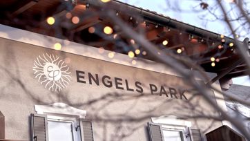 Nahaufnahme des Logos ENGELS PARK an der Fassade, umgeben von einem verschwommenen Zweig mit Lichtern.