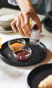 Hand reaching for chia pudding with raspberry at breakfast, next to jam, cheese and croissant.