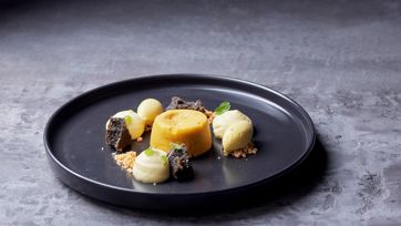 Kreativ angerichtetes Dessert mit Kuchen, Cremes und Crumbles auf schwarzem Teller.
