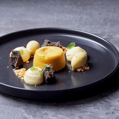 Kreativ angerichtetes Dessert mit Kuchen, Cremes und Crumbles auf schwarzem Teller.