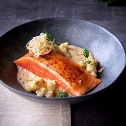 Gebratenes Lachsfilet mit Blumenkohl und Schaum, angerichtet mit Sauce und Gemüse.